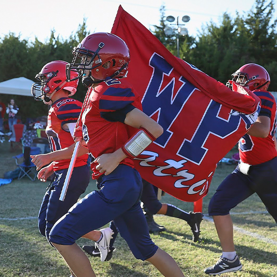 Football team running onto the field while waving a flag with their high school logo