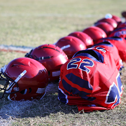 Football helmets and pads sitting in a row on a football field