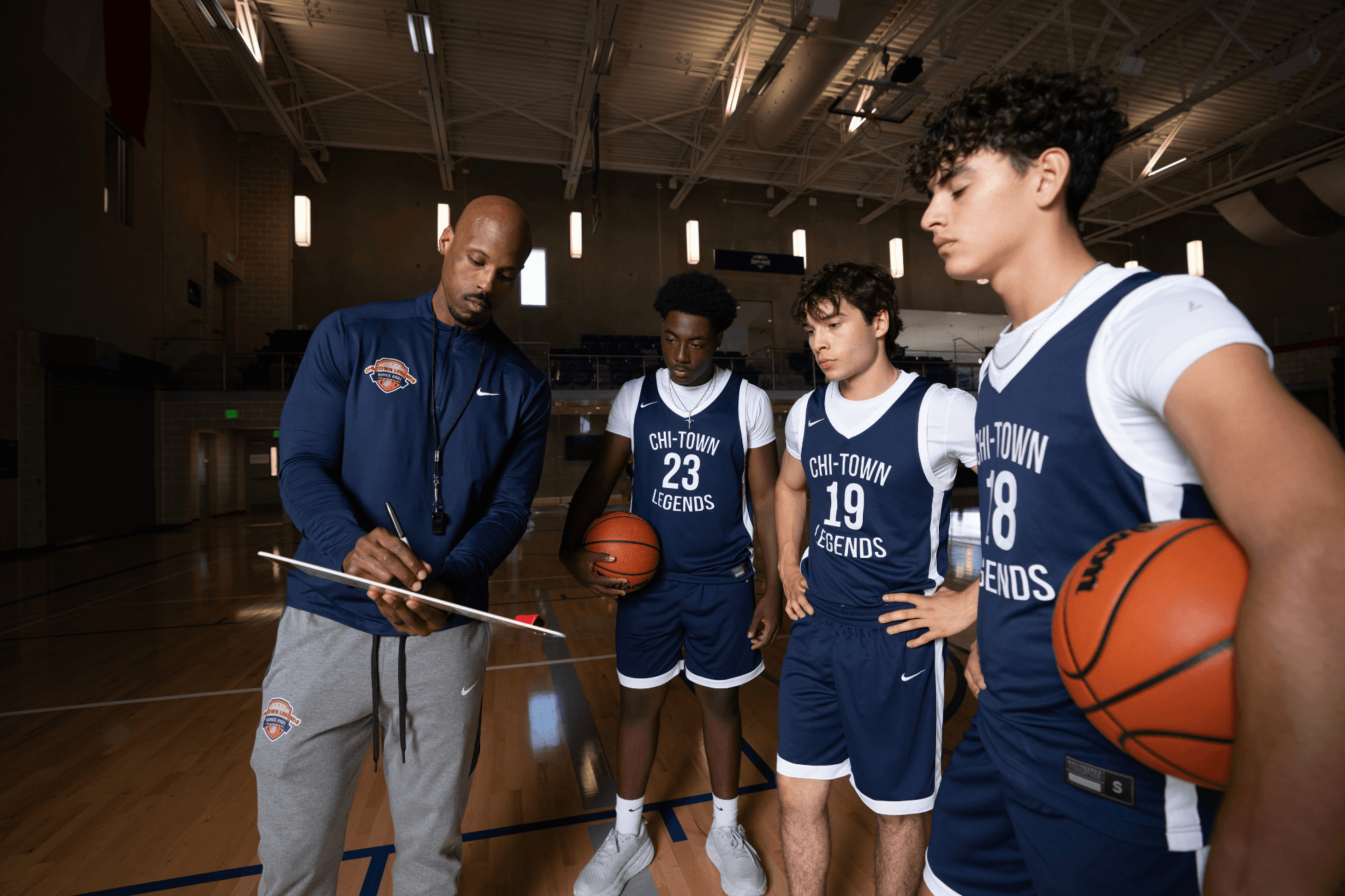a basketball coach writing on a clipboard in a huddle with players holding basketballs